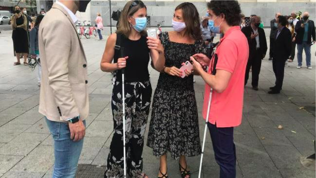 Dos personas usando un bastón para ciegos, hablando con otras dos personas.