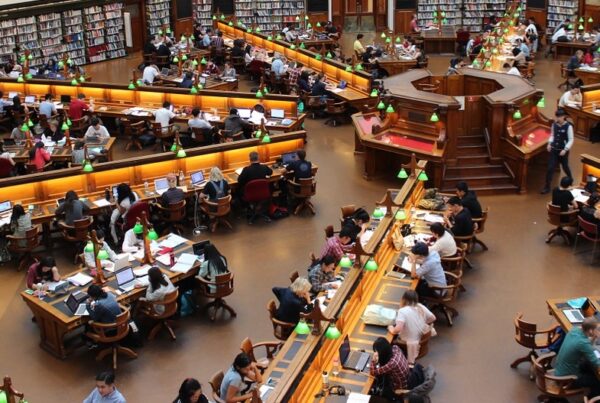 Biblioteca universitaria con mesas distribuidas formando una estrella. Hay muchos estudiantes