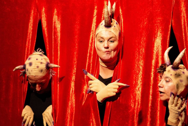 Fotografía de una obra de teatro accesible, con tres personas disfrazadas de animales con un telón rojo