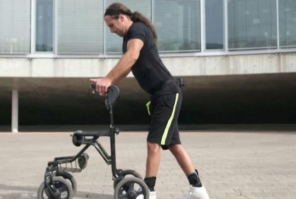 Hombre joven con ropa deportiva caminando apoyado en un carrito con ruedas