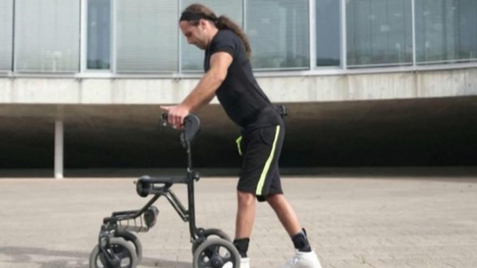 Hombre joven con ropa deportiva caminando apoyado en un carrito con ruedas