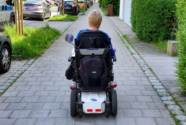 Mujer en silla de ruedas de espaldas, avanzando por una acera