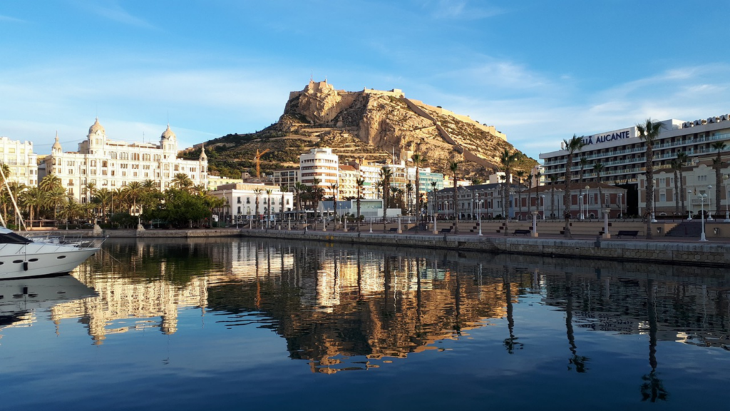 Fotografía de la ciudad de Alicante, con el mar, la línea de playa y el castillo al fondo