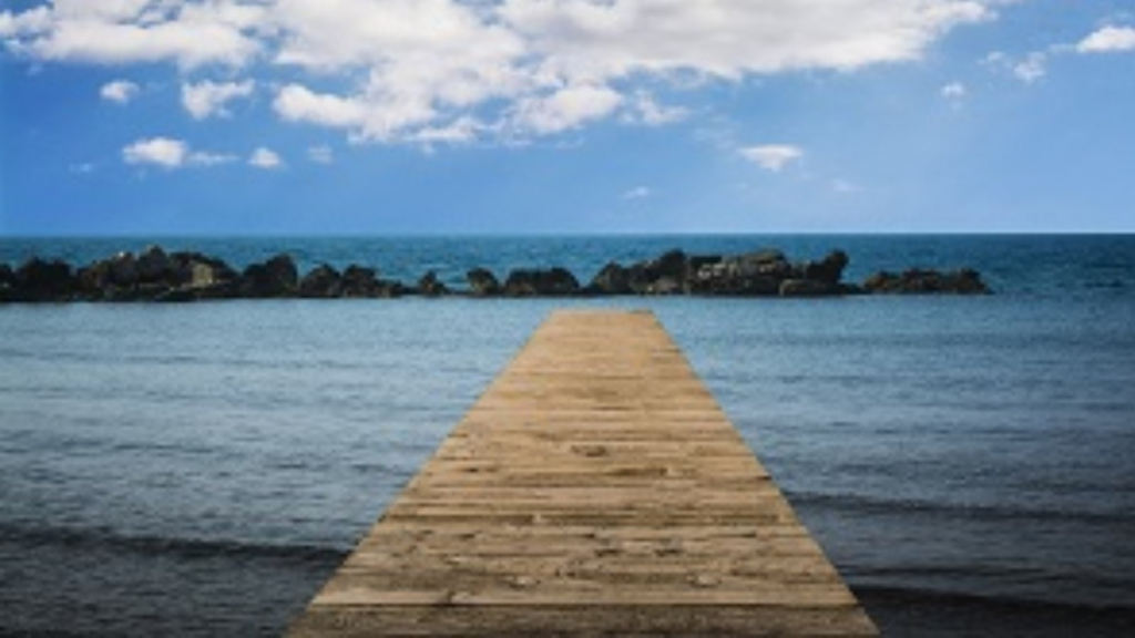 Fotografía de una pasarela de madera en una playa, que se dirige hasta el agua.