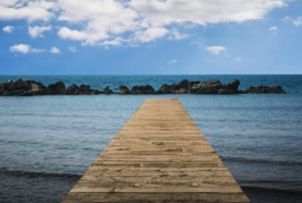 Fotografía de una pasarela de madera en una playa, que se dirige hasta el agua.