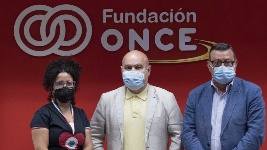 Fotografía de los representantes de Asemdis, CERMI y Fundación ONCE posando frente al logo de la Fundación ONCE sobre un fondo rojo oscuro