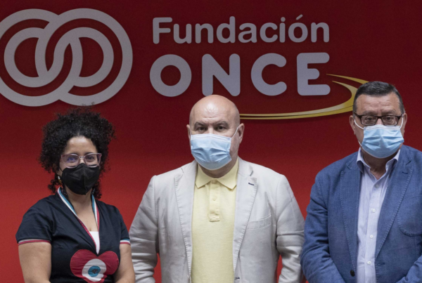 Fotografía de los representantes de Asemdis, CERMI y Fundación ONCE posando frente al logo de la Fundación ONCE sobre un fondo rojo oscuro