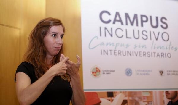 Fotografía de una intérprete de signos. En segundo plano, un cartel del campus inclusivo interuniversitario