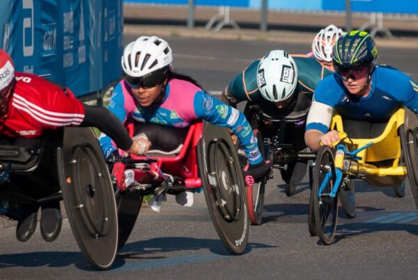 Personas en sillas de ruedas compitiendo en una carrera sobre una pista de asfalto