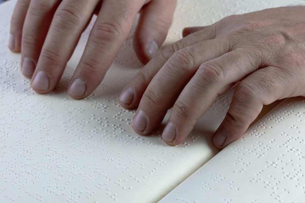 Manos de una persona joven leyendo un libro escrito en braille.