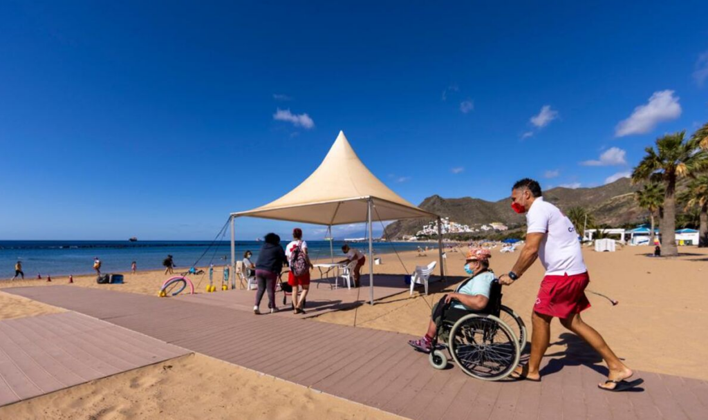 fotografía de una persona en silla de reudas atravesando la pasarela de madera en una playa.