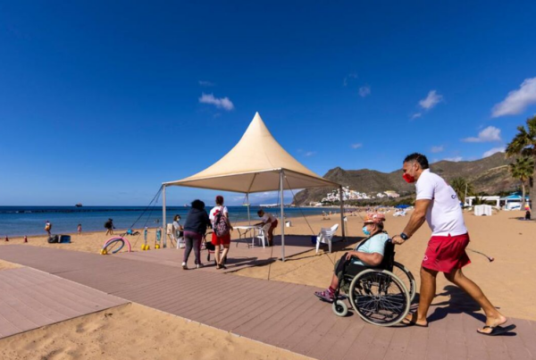 fotografía de una persona en silla de reudas atravesando la pasarela de madera en una playa.