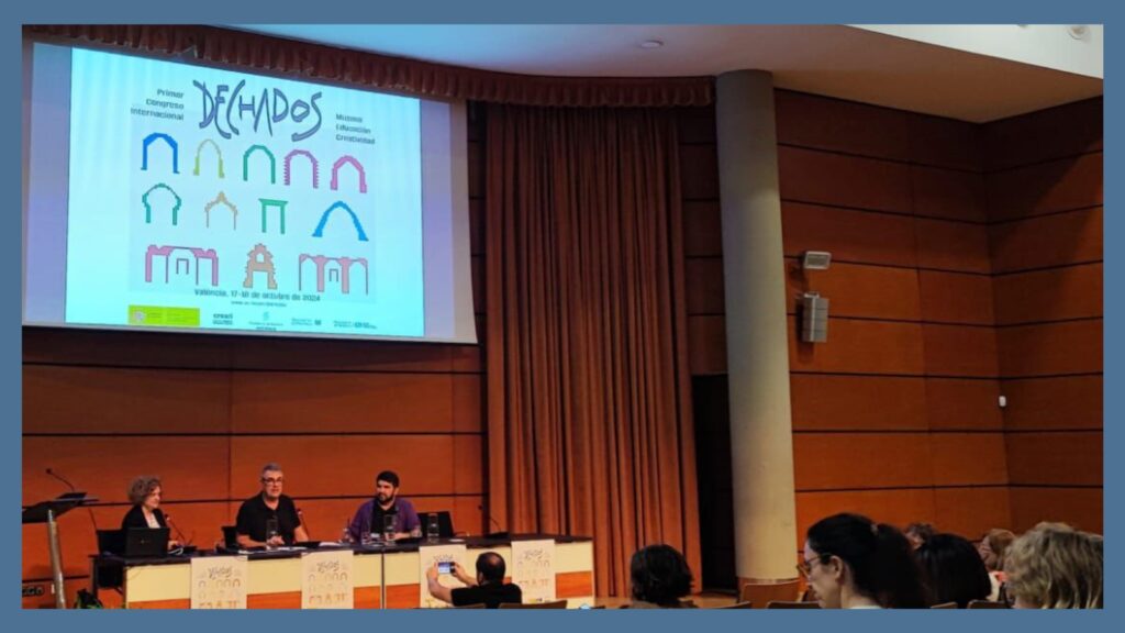 Fotografía de la mesa redonda del congreso DECHADOS, en la que participa nuestra directora, Chele esteve. Las tres personas están sentadas en una mesa con los carteles del congreso. Arriba, una pantalla donde se proyectan las presentaciones