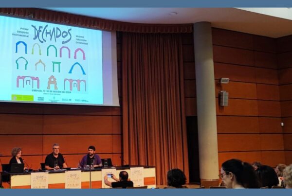 Fotografía de la mesa redonda del congreso DECHADOS, en la que participa nuestra directora, Chele esteve. Las tres personas están sentadas en una mesa con los carteles del congreso. Arriba, una pantalla donde se proyectan las presentaciones