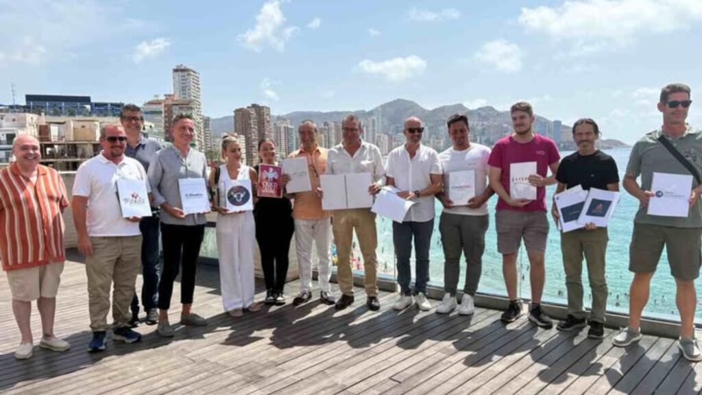 un grupo de hosteleros posa con sus cartas en braille, con la playa de fondo