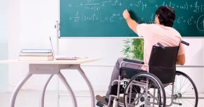 un profesor joven en silla de ruedas está escribiendo con tiza en una pizarra