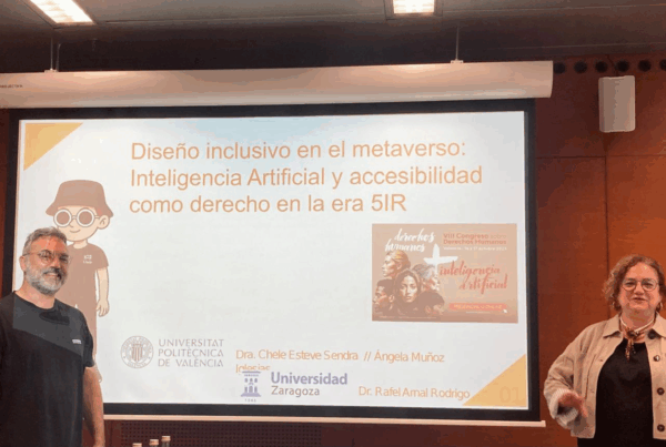 fotografía de chele esteve y rafal arnal tras su presentación en el congreso. Están de pie, en el escenario principal, a ambos lados de la proyección de la presentación en una gran pantalla.