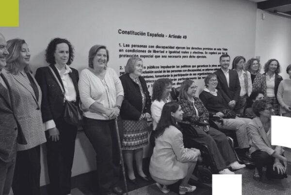 grupo de mujeres con discapacidad posando delante del texto del artículo 40 de la Constitución española escrito sobre la pared