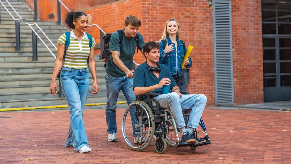Un grupo de cuatro estudiantes en la universidad, dos chicos y dos chicas. Uno de ellos va en silla de ruedas.