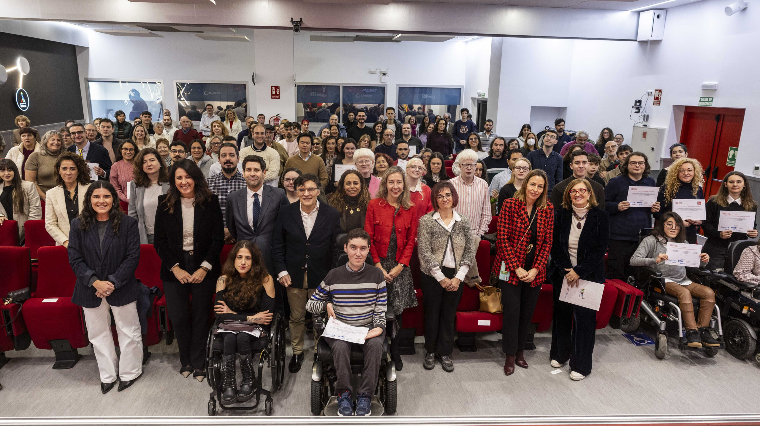 fotografía de la sala con los participantes en el acto de entrega de las becas. Están todos mirando a la cámara.