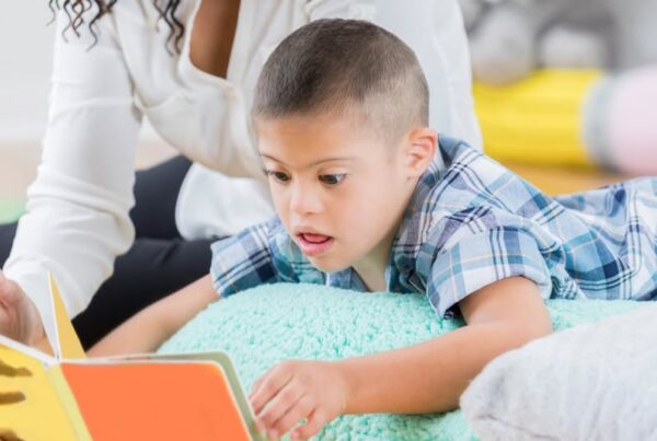 un niño con síndrome de down tumbado en su cama leyendo un libro