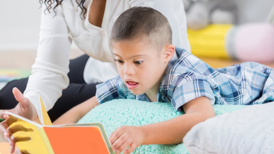 un niño con síndrome de down tumbado en su cama leyendo un libro