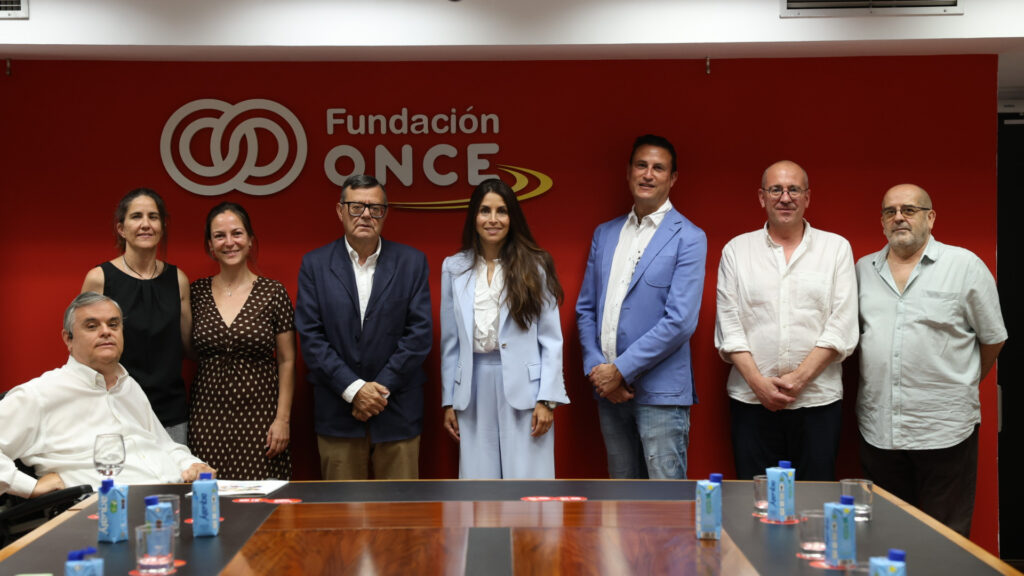 Representantes de Fundación ONCE y UPV en evento sobre accesibilidad digital UPV, frente a un cartel rojo institucional, promoviendo la inclusión y la accesibilidad digital universitaria.