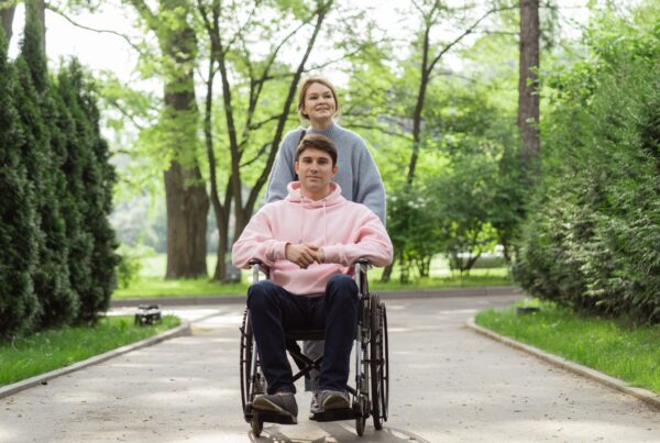 Una pareja joven, él va en silla de ruedas, está paseando por un parque