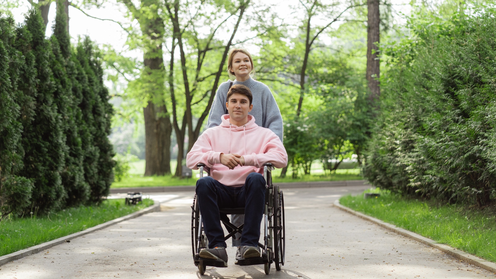 Una pareja joven, él va en silla de ruedas, está paseando por un parque