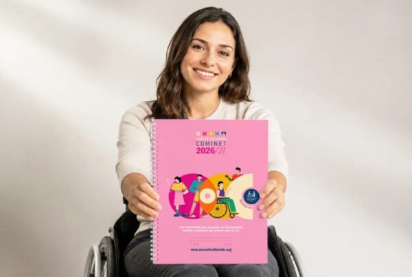 Una mujer joven en silla de ruedas enseña a cámara la portada de la guía